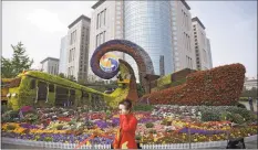  ?? Andy Wong / Associated Press ?? In this April 23, 2019, photo, a woman walks by workers on a platform put finishing touch on a flowers decoration in a shape of a train and a container vessel for promoting the upcoming Belt and Road Forum in Beijing.