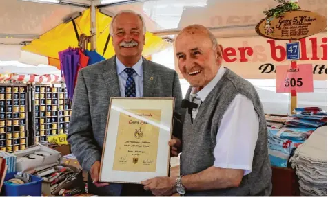  ?? Foto: Denis Dworatsche­k ?? Hermann Faul (links) überreicht Georg Huber eine Ehrenurkun­de zu seinem 70 jährigen Jubiläum auf der Nördlinger Mess’. Der 82 Jährige betreibt den Marktstand „Der bil lige Jakob“.