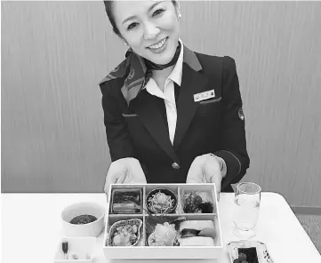  ??  ?? A JAL cabin attendant shows Japanese in-flight meals supervised by Chef Jun Kurogi, at the JAL Royal Catering Co. Haneda facility in Tokyo on Friday.