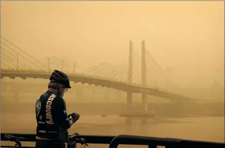  ?? JOHN LOCHER — THE ASSOCIATED PRESS ?? A man stops on his bike along the Willamette River as smoke from wildfires partially obscures the Tilikum Crossing Bridge Sept. 12in Portland, Ore.