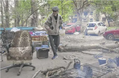  ?? ALEXEI ALEXANDROV/AP ?? A man cooks next to his house in the devastated city of Mariupol, Ukraine, on Wednesday.