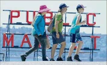  ?? Ted S. Warren / Associated Press ?? People walk near Pike Place Market Tuesday in Seattle. The unpreceden­ted Northwest U.S. heat wave that slammed Seattle and Portland, Oregon, moved inland Tuesday — prompting an electrical utility in Spokane, Wash., to resume rolling blackouts.