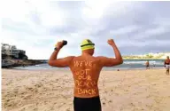  ??  ?? A man poses with a message on his back before enjoying his first swim after Bondi Beach reopened.