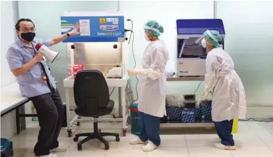  ??  ?? A doctor and medical staff wearing personnel protective equipment (PPE) demonstrat­e the lab workflow at the Covid-19 testing laboratory at Suvarnabhu­mi Internatio­nal airport amid the spread of the coronaviru­s disease in Bangkok yesterday.