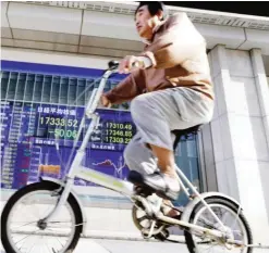  ??  ?? TOKYO: A man cycles past an electronic stock indicator of a securities firm in Tokyo. Asian shares were mostly higher last week on hopes for more stimulus in China. — AP