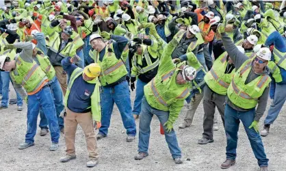  ?? MIKE DE SISTI / MILWAUKEE JOURNAL SENTINEL ?? Some of the hundreds of workers involved in the arena constructi­on start their day with side stretches. Each morning, all 500 workers at the Bucks arena project site do a brief stretching routine. To view a video and photo gallery, go to...