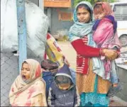  ?? AFP ?? A migrant worker and children wait at a bus stand in Srinagar on Monday.