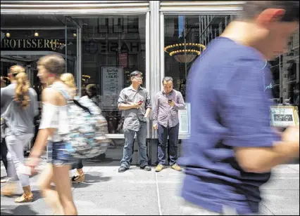  ?? BENJAMIN NORMAN / THE NEW YORK TIMES ?? Richard Leong (background, left) and his co-worker Wai Lam play “Pokémon Go” on their lunch break, outside the Empire State Building in Manhattan. When undertaken as a slow game, “Pokémon Go” can soothe rather than excite — accessing a different part...