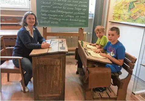  ?? Foto: Jörg Sigmund ?? „Probesitze­n“auf alten Schulbänke­n: Lehrerin Katharina Friedrich Scharunge sowie Raphael Glaß und Leon Gundel (von links) aus der Klasse 3 a.