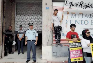  ??  ?? Police officers stand guard at the entrance of the Interior Ministry offices in Athens yesterday as Afghan migrants stage a protest demanding rights as refugees fleeing war. Unlike most Syrians, Afghans are no longer guaranteed asylum.