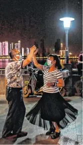  ?? HECTOR RETAMAL, GETTY IMAGES ?? Dancing in the moonlight:
A couple wearing face masks dance in a park next to the Yangtze River in Wuhan