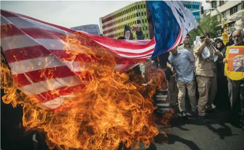  ?? (Tasmin News Agency/Reuters) ?? IRANIANS BURN a US flag during a protest in Tehran on Friday against President Donald Trump’s decision to exit the 2015 nuclear deal.