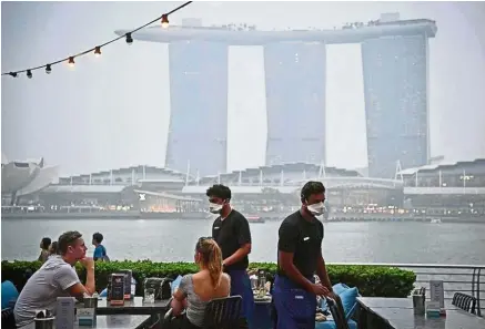  ?? — The Straits Times/ANN ?? Masked service: Waiters serving customers at OverEasy in Fullerton Road in Singapore. Restaurant­s with al fresco dining say customers have been staying away since last weekend.