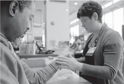  ?? KARL MERTON FERRON/BALTIMORE SUN ?? A device is applied to the injured hand of Sgt. Keith Mcneill by senior hand therapist Lauren Davis, as he undergoes continued rehabilita­tion at Union Memorial Hospital after being shot in 2014.