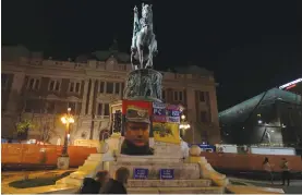  ?? — AP ?? People walk in front of the monument of late Serbian Duke, Mihailo Obrenovic, arranged with picture of former Bosnian Serb wartime general Ratko Mladic and a banner reading: ‘ Serbs and Russians — brothers forever’ in Belgrade, Serbia, on Wednesday.
