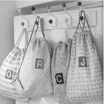  ??  ?? These pretty personaliz­ed drawstring bags hung from hooks are ideal for holding hats and scarves for each family member.