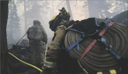  ?? AP PHOTO/JAE C. HONG ?? Two firefighte­rs from Cosumnes Fire Department carry water hoses while holding a fire line to keep the Caldor Fire from spreading in South Lake Tahoe, Calif., on Friday.