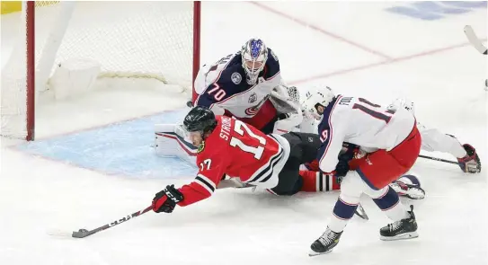  ?? STACY REVERE/GETTY IMAGES ?? Blackhawks center Dylan Strome tries to gain control of the puck while falling to the ice Friday in front of Blue Jackets goalie Joonas Korpisalo.