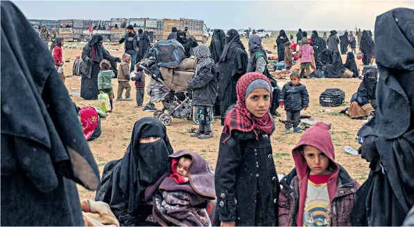  ??  ?? Women and their children wait to be transporte­d to a refugee camp