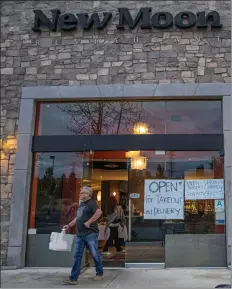  ?? Bobby Block/The Signal ?? A customer leaves New Moon Restaurant, on Newhall Ranch Road, carrying a to-go container Monday evening. Though restaurant­s have been ordered not to allow sit-down dining, many are open, offering takeout and delivery services.