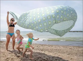  ??  ?? Maggie Giles, of Erie, lifts a bed sheet as her daughters Olenna, 5, and Aria, 3, play Friday at Presque Isle State Park.