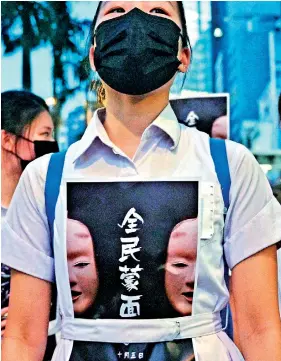  ??  ?? High school students chant slogans as they stick posters reading “all people masked” on their uniforms as they gather in the heart of Hong Kong's commercial district on Friday, after the government announced a ban on facemasks. AFP