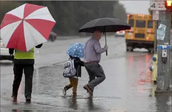  ?? John Walker/The Fresno Bee via AP of ?? As the rain falls, a man walks his son to Garfield Elementary through a flooded section Peach and Need avenues on Monday in Clovis, Calif. The powerful storm that walloped Northern California over the weekend moved into Southern California on Monday, carrying with it the potential for localized flooding, strong winds and debris flows across the region.