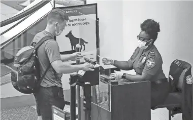  ?? JOHN RAOUX/AP ?? A traveler at Orlando Internatio­nal Airport lowers his mask so a TSA officer can compare his face to his ID. A TSA official says the agency withheld masks from workers early during the pandemic.