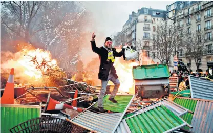  ?? ?? National malaise: a demonstrat­or stands on a burning barricade during an anti-government ‘yellow vest’ protest in Paris, in January 2019