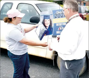  ?? (NWA Democrat-Gazette/Mike Eckels) ?? After picking up her cap and gown, Paige Barrett looks at the lawn sign given to her by Toby Conrad, Decatur High School principal, during senior cap and gown pickup day in the high school parking lot May 7.