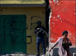  ?? — AFP photo ?? A woman walks past an armed police officer monitoring a street after gang violence in the neighborho­od on the evening of in Port-au-Prince, Haiti.