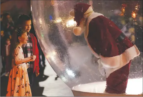  ?? (The Oklahoman/Doug Hoke) ?? A young girl and boy visit with the Santa in a snow globe during Automobile Alley’s Lights on Broadway in Oklahoma City.