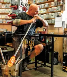  ??  ?? Will blows the molten glass while sitting in the chair he made especially for the job, using the metal arms to rest the blowing iron on.