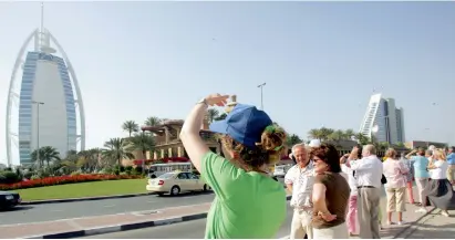  ?? — AFP ?? Tourists take pictures of the Burj Al Arab and Jumeirah Beach Hotel in Dubai. Hotel room rates and occupancy have been stable.