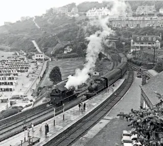  ??  ?? Sea, sand and steam: On a wet August 4, 1961, GWR 2-6-2T No. 4570 enters St Ives station with the 1.30pm from St Erth, while another member of the class, believed to be No. 4549, waits on the adjacent track. The signalman has collected the single line token and is walking towards his signalbox on the right past a camping coach. In the middle distance, partly obscured by the light engine's smoke, is St Ives' small engine shed. Row upon row of beach tents are on the resort's Porthminst­er beach, and just visible on platform lampposts are totem station signs, one nearest the photograph­er and another further along the platform, close to the approachin­g train from St Erth. Perhaps it is one of this pair that will be making its auction debut at the GW Railwayana sale on July 24. TRANSPORT TREASURY/PETER GRAY