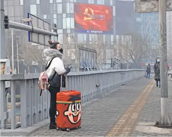  ?? NG HAN GUAN/ AP ?? A traveler stands near a display showing government propaganda in the fight against the coronaviru­s in Beijing on Thursday. China is struggling to contain the virus.