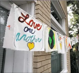  ?? The Associated Press ?? ‘LOVE ONE ANOTHER’:Painted cloth flags including one saying "Love One Another" are strung across a store Thursday along Mt. Vernon Ave. in Alexandria, Va., as FBI agents continue to investigat­e the scene nearby the day after House Majority Whip Steve...