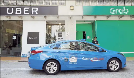  ?? REUTERS ?? A taxi passes Uber and Grab offices in Singapore over the weekend. Uber has pulled out of Southeast Asia, selling operations to rival Grab. Uber and Grab Philippine­s addressed users yesterday, announcing that the merger’s transition would be complete...