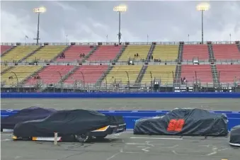  ?? AP PHOTO/GREG BEACHAM ?? Covered cars from the NASCAR Xfinity Series sit parked on pit road at Auto Club Speedway during a rain delay before the planned start of Saturday’s race in Fontana, Calif. NASCAR canceled practice and qualifying sessions and ultimately postponed the race to Sunday night because of ongoing heavy rains.