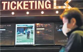  ?? — AFP photo ?? A man walks past a screen showing a poster of Bong Joon-ho’s film ‘Parasite’ at a cinema in Seoul.