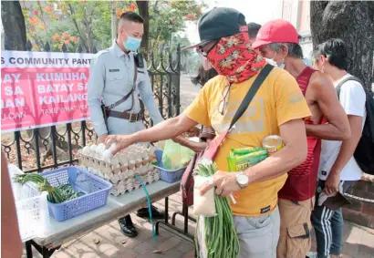  ?? PHOTOGRAPH BY JOEY SANCHEZ MENDOZA FOR THE DAILY TRIBUNE ?? STAFF of the Intramuros Administra­tion assist residents in taking their pick of fresh produce at a community pantry set up in front of the Manila Cathedral, inspired after a similar initiative in Maginhawa Street.