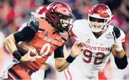  ?? EMILEE CHINN/GETTY ?? Cincinnati’s Desmond Ridder carries the ball past Houston’s Logan Hall #92 in the AAC title game Saturday at Nippert Stadium in Cincinnati, Ohio.