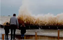  ?? — AFP ?? A man and children watch waves crashing against a tidal wall on Thursday in Asnelles, Northweste­rn France, after Storm Eleanor swept into Europe.