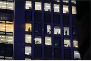  ?? (AP) ?? A man looks out of the window in December at an office building in Frankfurt, Germany. A new report says climate commitment­s by companies aren’t always as green as they seem.