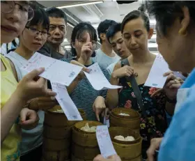  ?? — AFP ?? In this photo taken on August 7, a customer ( centre) gestures to choose her dish as other diners hold their order sheets in order to catch the attention of an employee ( right) while they crowd around her trolley of bamboo steamers containing freshly steamed dim sum dishes at the Lin Heung Tea House in Hong Kong.