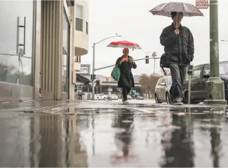  ?? Jessica Christian / The Chronicle ?? Pedestrian­s with umbrellas walk along Grand Avenue in Oakland during a heavy rainstorm. Rain is expected to tail off Friday.