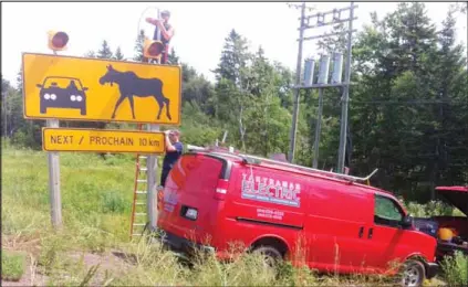  ?? SUBMITTED ?? Travis Smart and David Jury of Tantramar Electric install flashing lights on the moose crossing sign in the Melrose area in August 2012. At the time, increased efforts were underway to reduce the number of moose-vehicle collisions in the area after three people – including a Cape Tormentine couple and a man from Charlottet­own, P.E.I. – were killed.