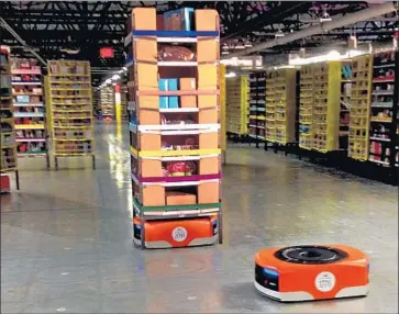  ?? Brandon Bailey Associated Press ?? A KIVA robot drive unit, right, is seen before it moves beneath a stack of merchandis­e pods during a 2014 tour of one of Amazon’s distributi­on centers in Tracy, Calif. The retail giant is replacing people with software.