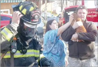  ?? Keith Bryant/The Weekly Vista ?? Firefighte­r-EMT Justin Tesreau, left, starts to remove his helmet after handing Runt, who was still in the house during the fire, back to his owners, Amber and Timothy McKinney.