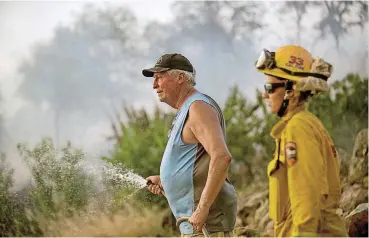  ?? [AP PHOTO] ?? Jim Berglund sprays water Saturday while defending his home near Oroville, Calif., as a wildfire approaches. Although flames leveled Berglund’s barn, his home remained unscathed as the main fire passed.